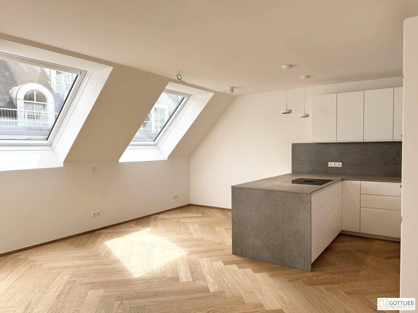 Moderne offene Küche mit Kochinsel, weißen Schränken und Fischgrätparkett unter Dachfenstern.