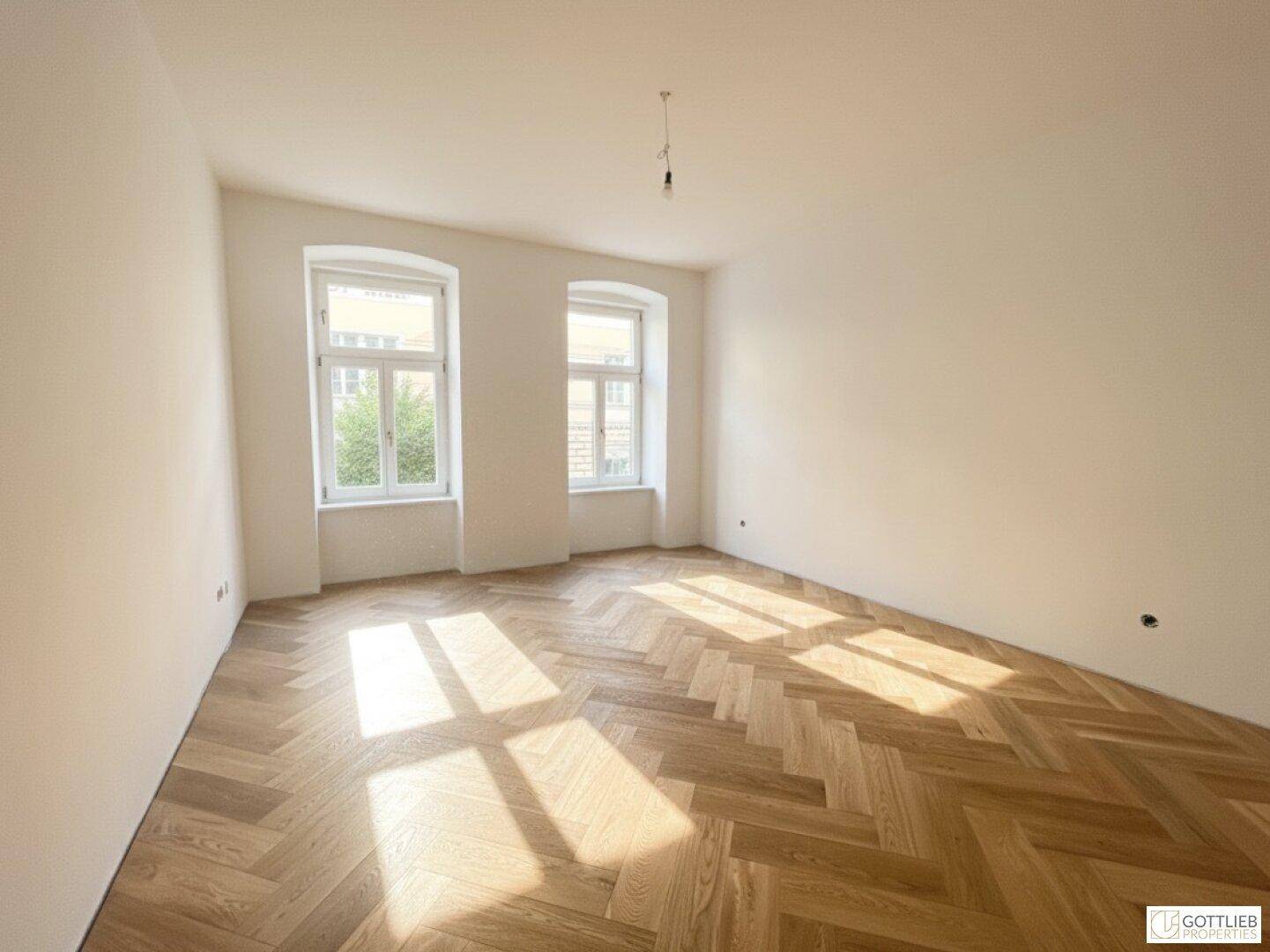 Lichtdurchfluteter Raum mit elegantem Fischgrätparkett und hohen Decken, ideal für Wohnzwecke.