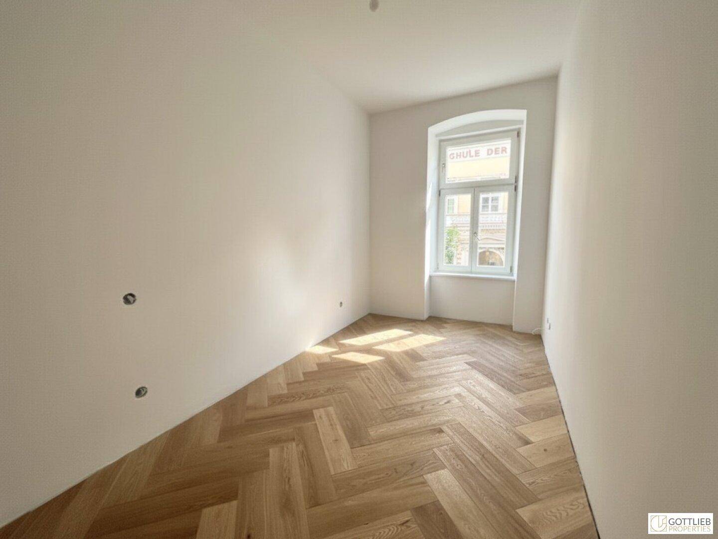 Gemütliches Zimmer mit Fischgrätparkett und einem großen Fenster, ideal als Schlaf- oder Arbeitszimmer.