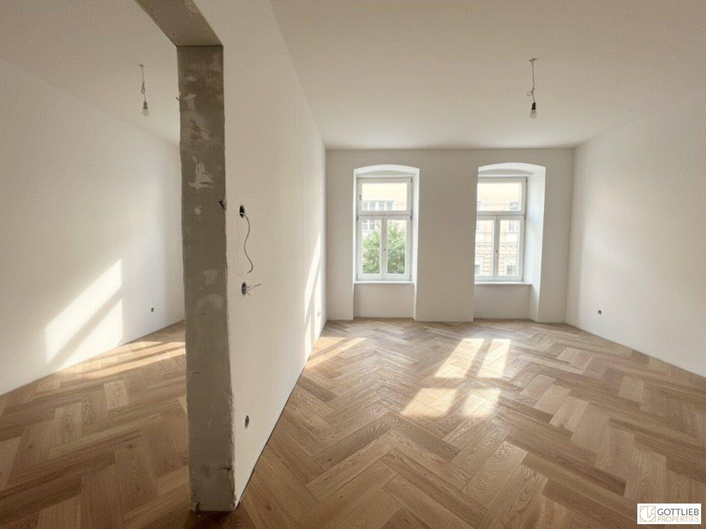 Geräumiger Wohnbereich mit Fischgrätparkett und viel Tageslicht, ideal für offenes Wohnen.