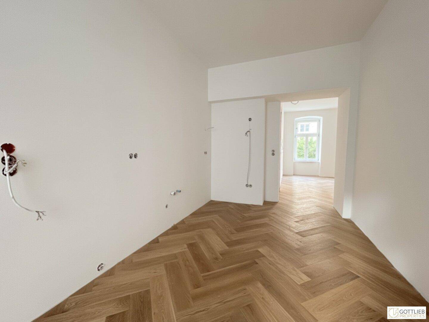 Heller Flur mit Fischgrätparkett, der zu weiteren Räumen mit großen Fenstern führt.