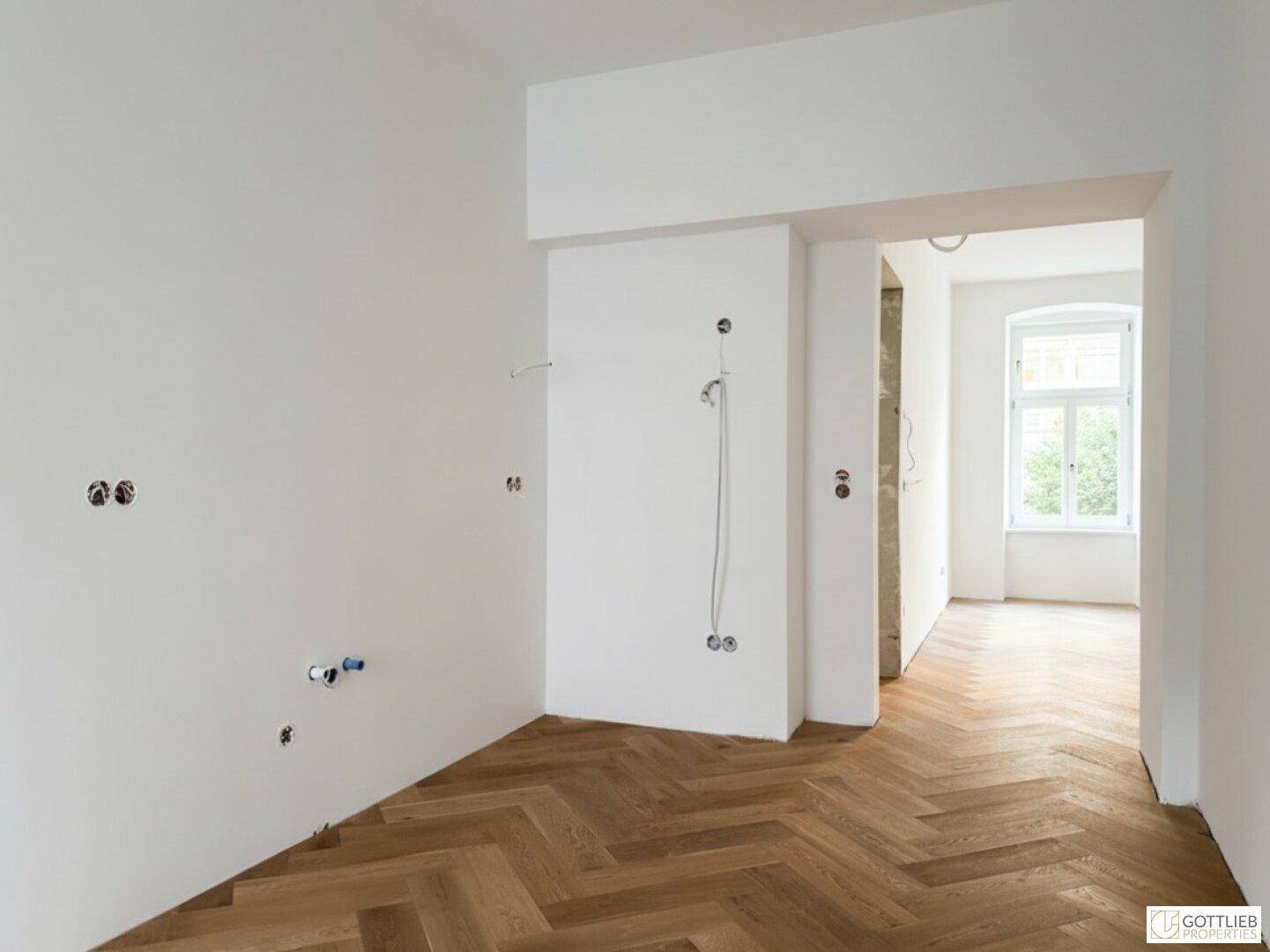 Rohbauküche mit Fischgrätparkett und vorbereiteten Anschlüssen, bereit für die Installation.