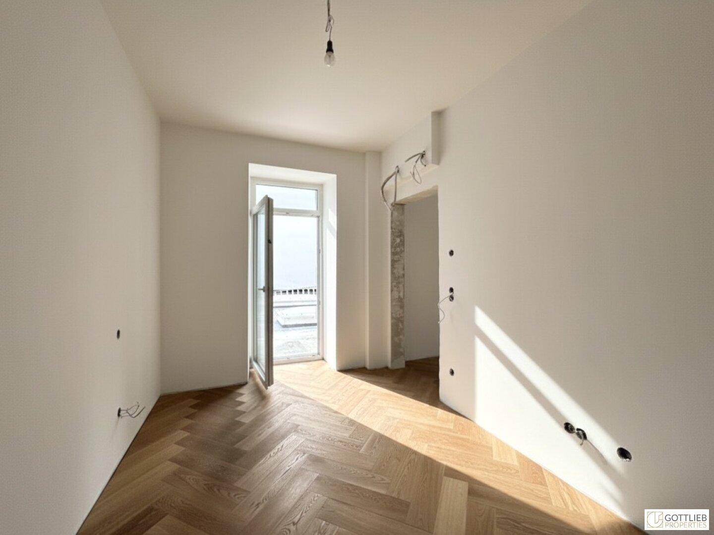 Zimmer mit Fischgrätparkett und Zugang zu einem Balkon, bietet viel natürliches Licht.