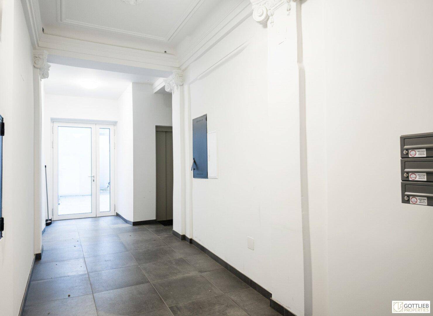 Heller Eingangsbereich mit Fliesenboden, Stuckelementen an der Decke und Zugang zum Aufzug.