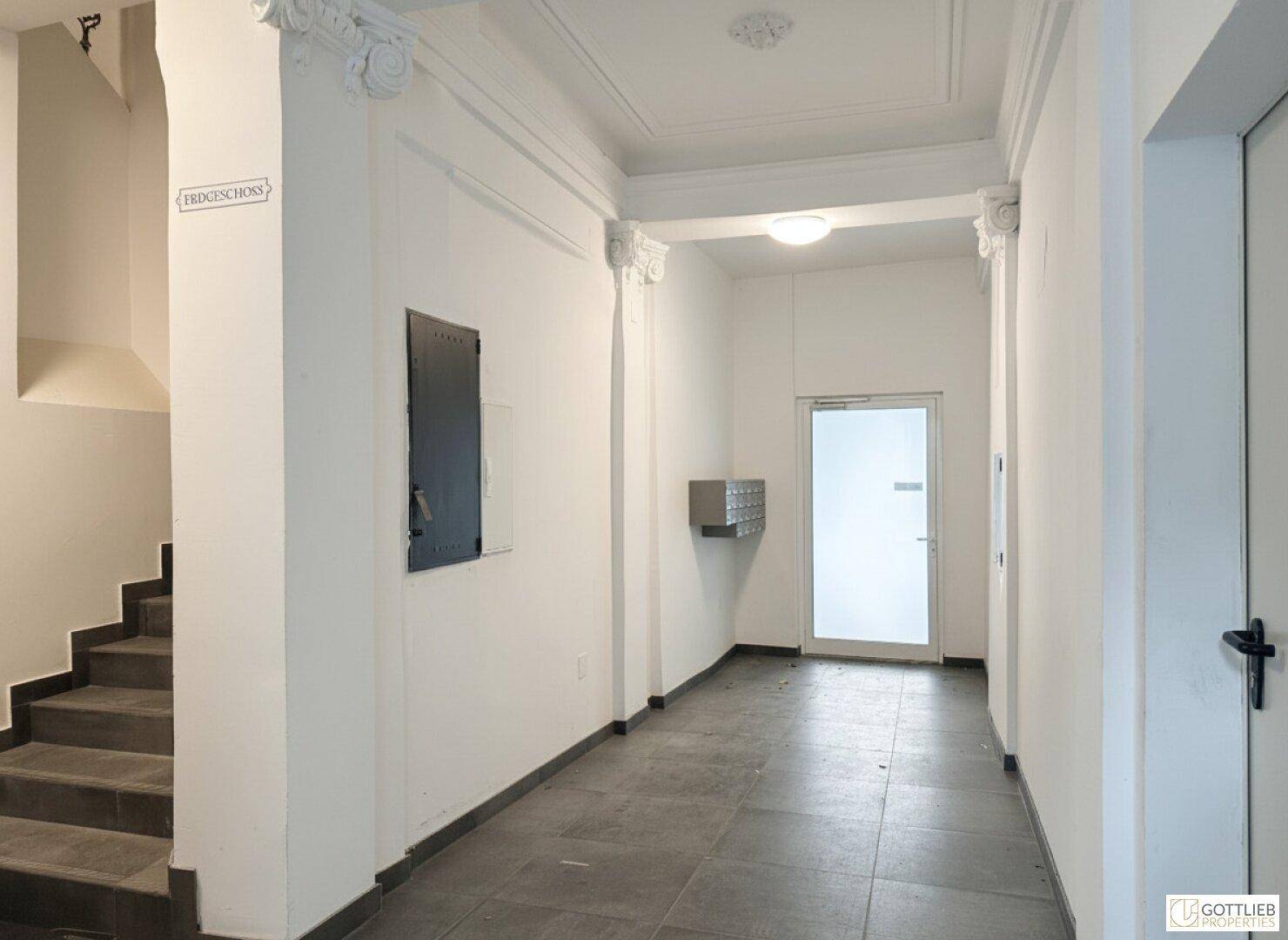 Eingangsbereich mit Fliesenboden, Stuckdecke und Zugang zum Treppenhaus und Briefkästen.