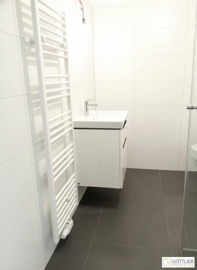 Modernes Badezimmer mit weißen Fliesen, schwebendem Waschtisch und Handtuchheizkörper.