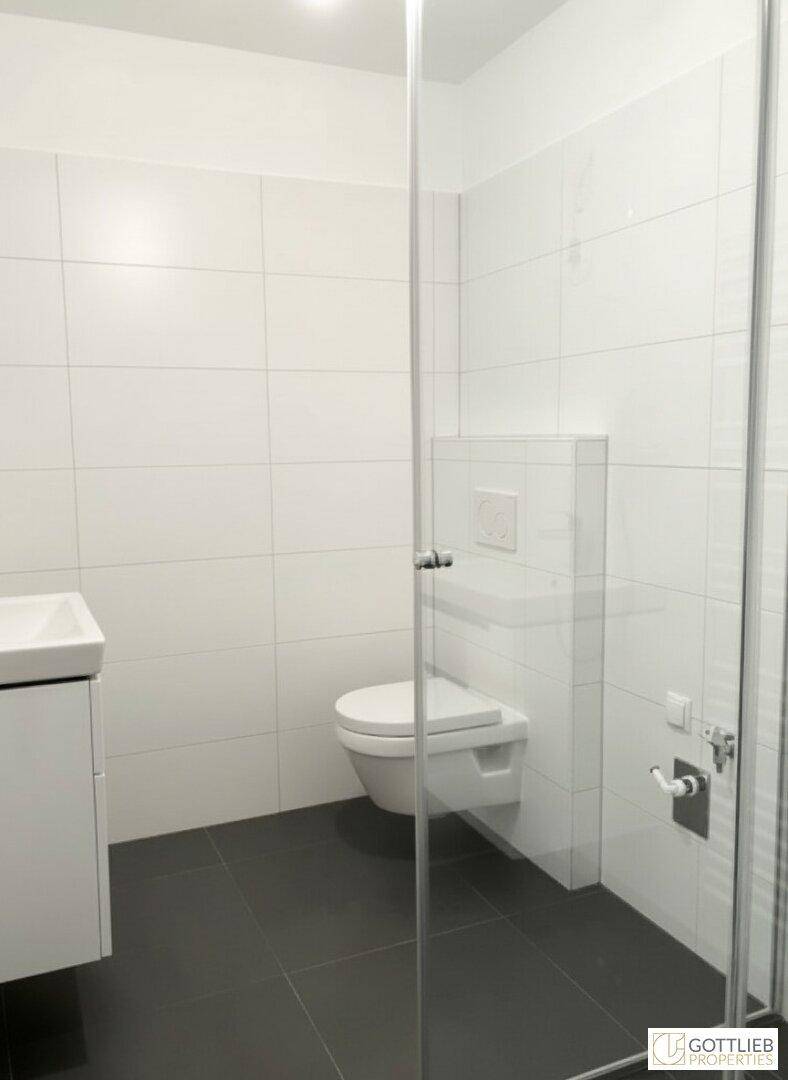 Zeitgemäßes Badezimmer mit wandhängendem WC, weißen Fliesen und Glasduschwand.