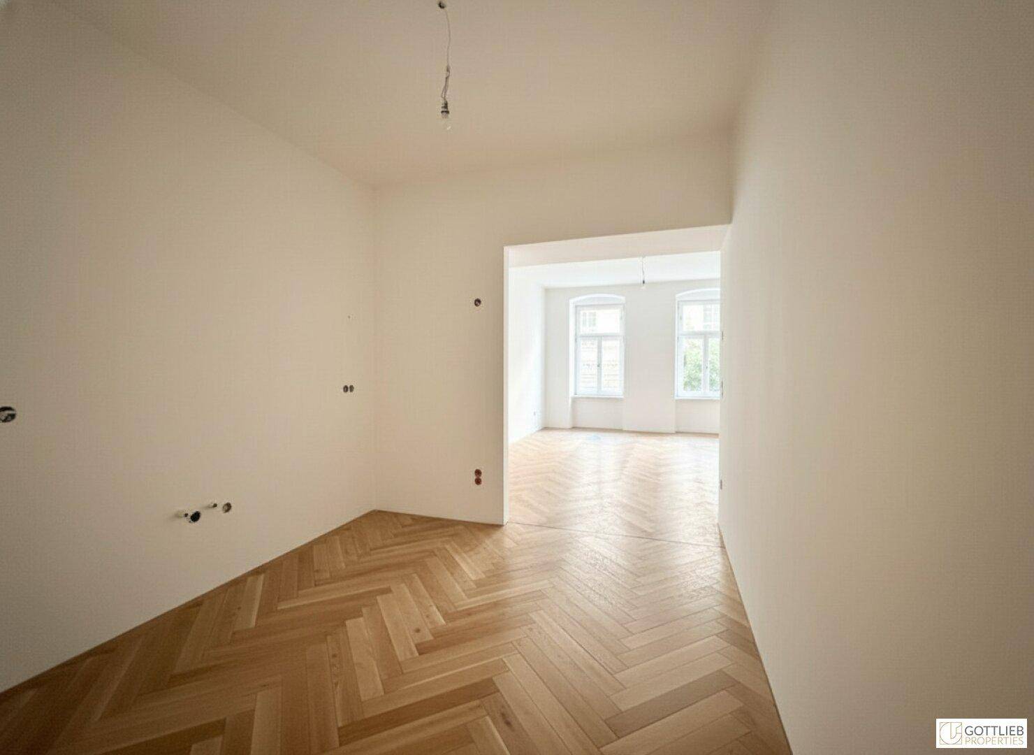 Heller Raum mit Fischgrätparkett, der zu einem weiteren Zimmer führt.