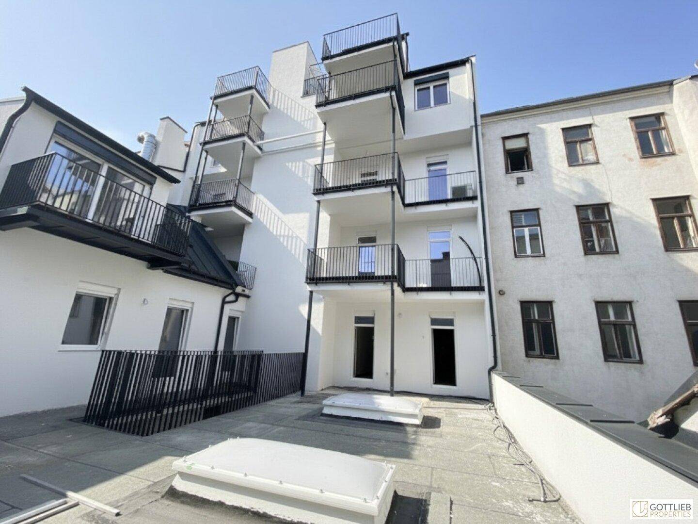 Rückfassade eines Gebäudes mit mehreren Balkonen und einer Dachterrasse im Vordergrund.