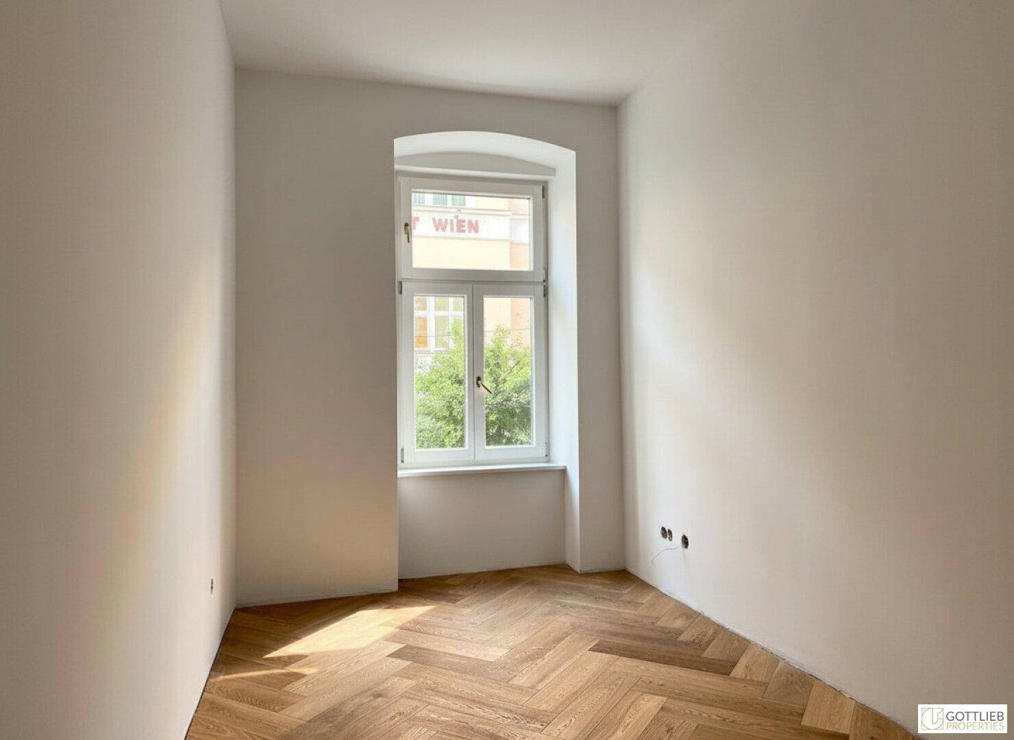 Gemütliches Zimmer mit Fischgrätparkett und einem großen Fenster, das den Raum erhellt.
