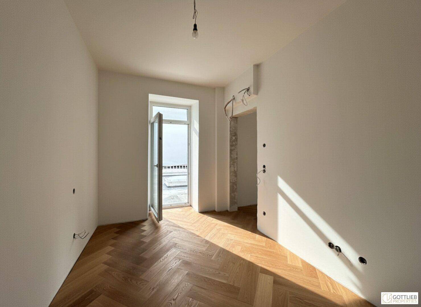 Helles Zimmer mit Fischgrätparkett und Zugang zu einem Balkon, der viel Licht bietet.