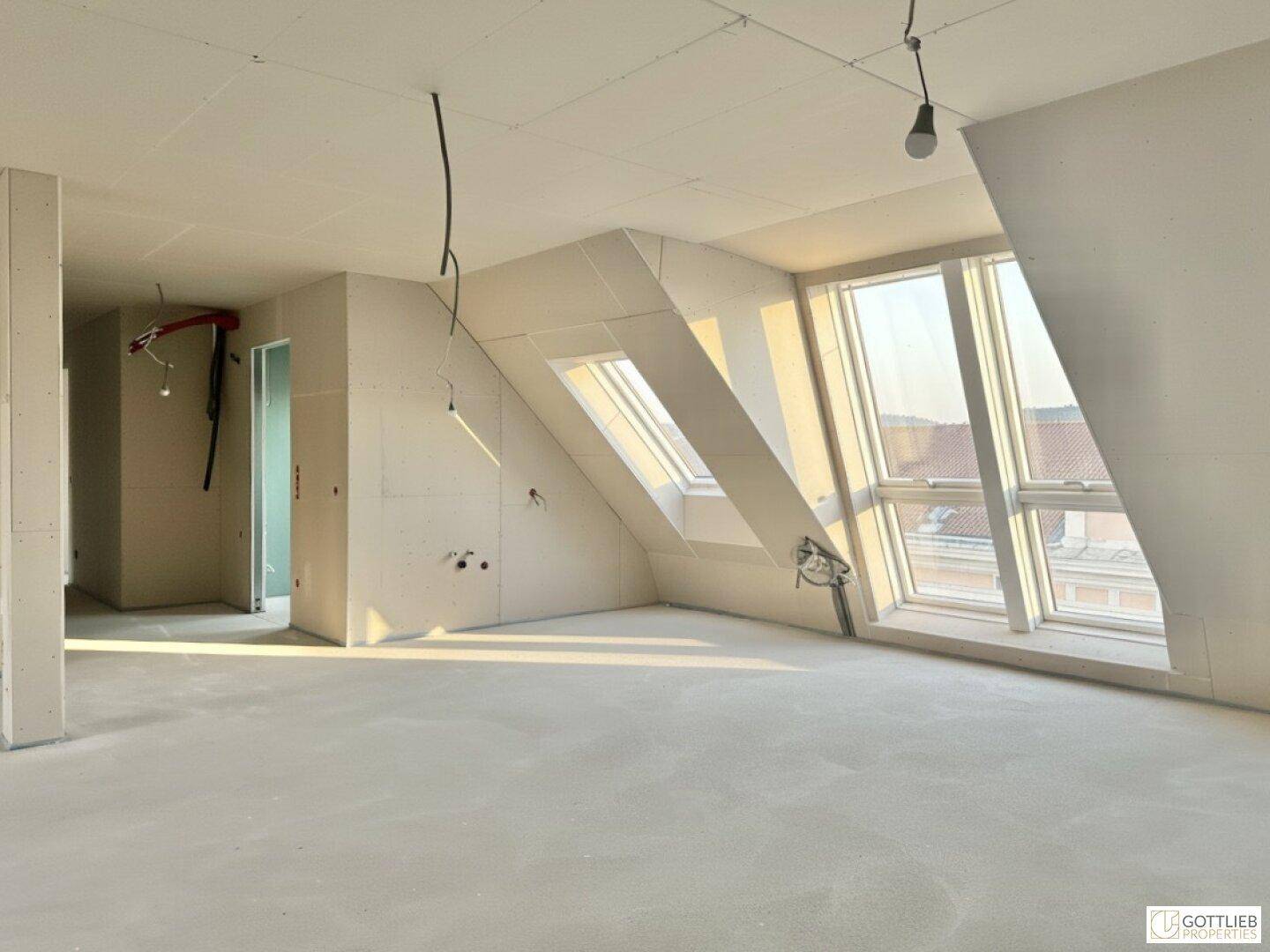 Geräumiger Dachgeschossraum im Rohbau mit schrägen Wänden und großen Fensterflächen.