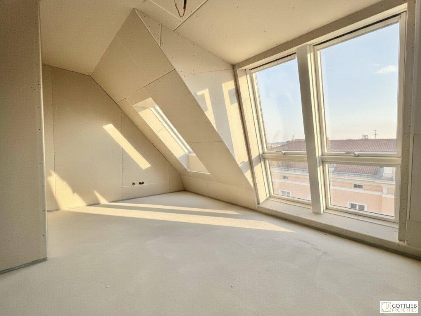 Heller Dachgeschossraum im Rohbau mit schrägen Wänden und viel natürlichem Lichteinfall.