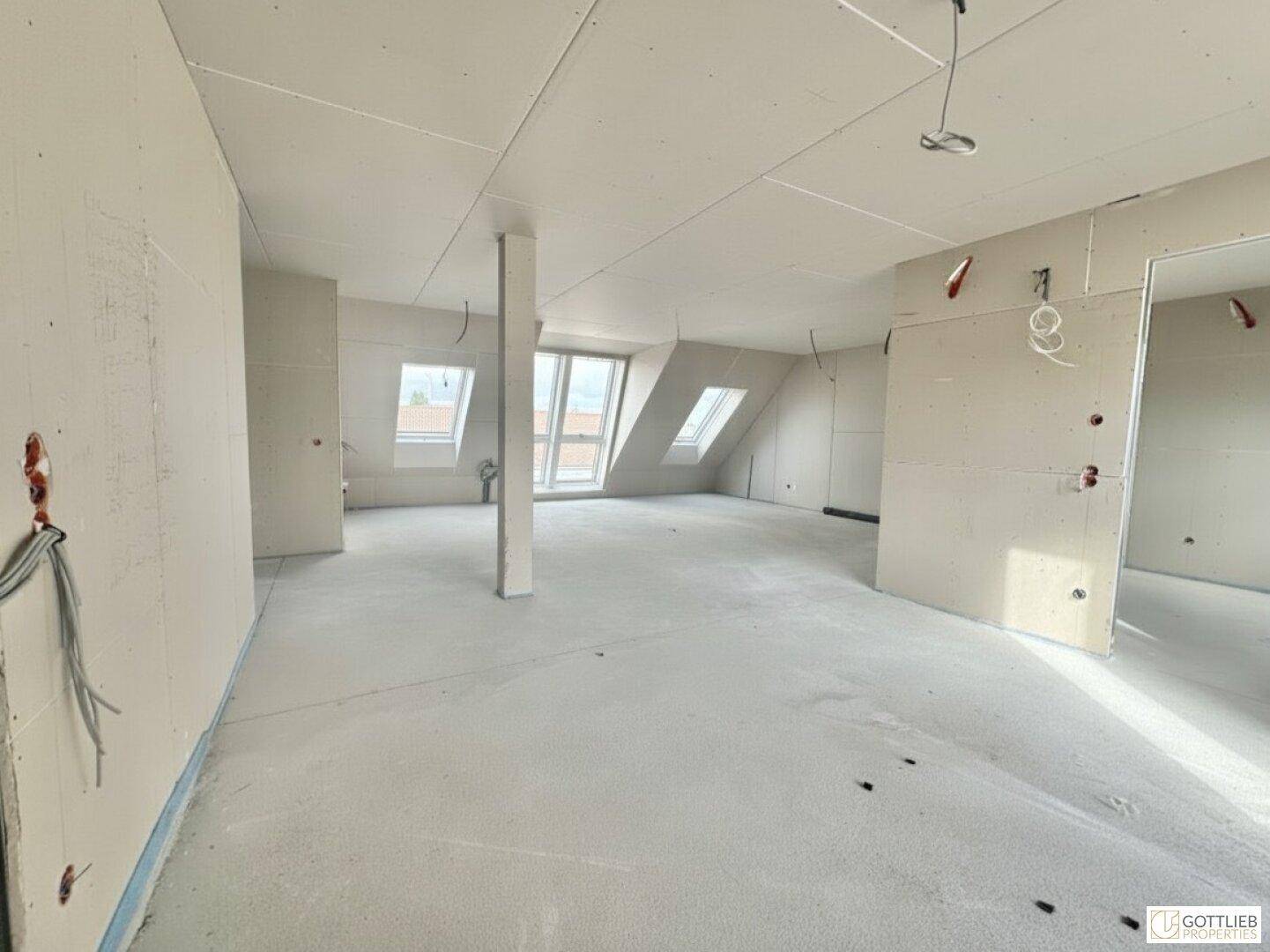 Unfertiger Dachgeschossraum mit Trockenbauwänden, schrägen Decken und vorbereiteten Installationen.