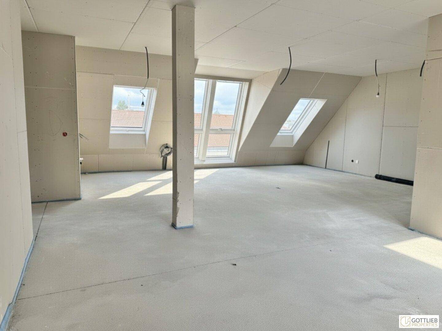 Geräumiger Dachgeschossraum im Rohbau mit Stütze, schrägen Wänden und hellen Dachfenstern.