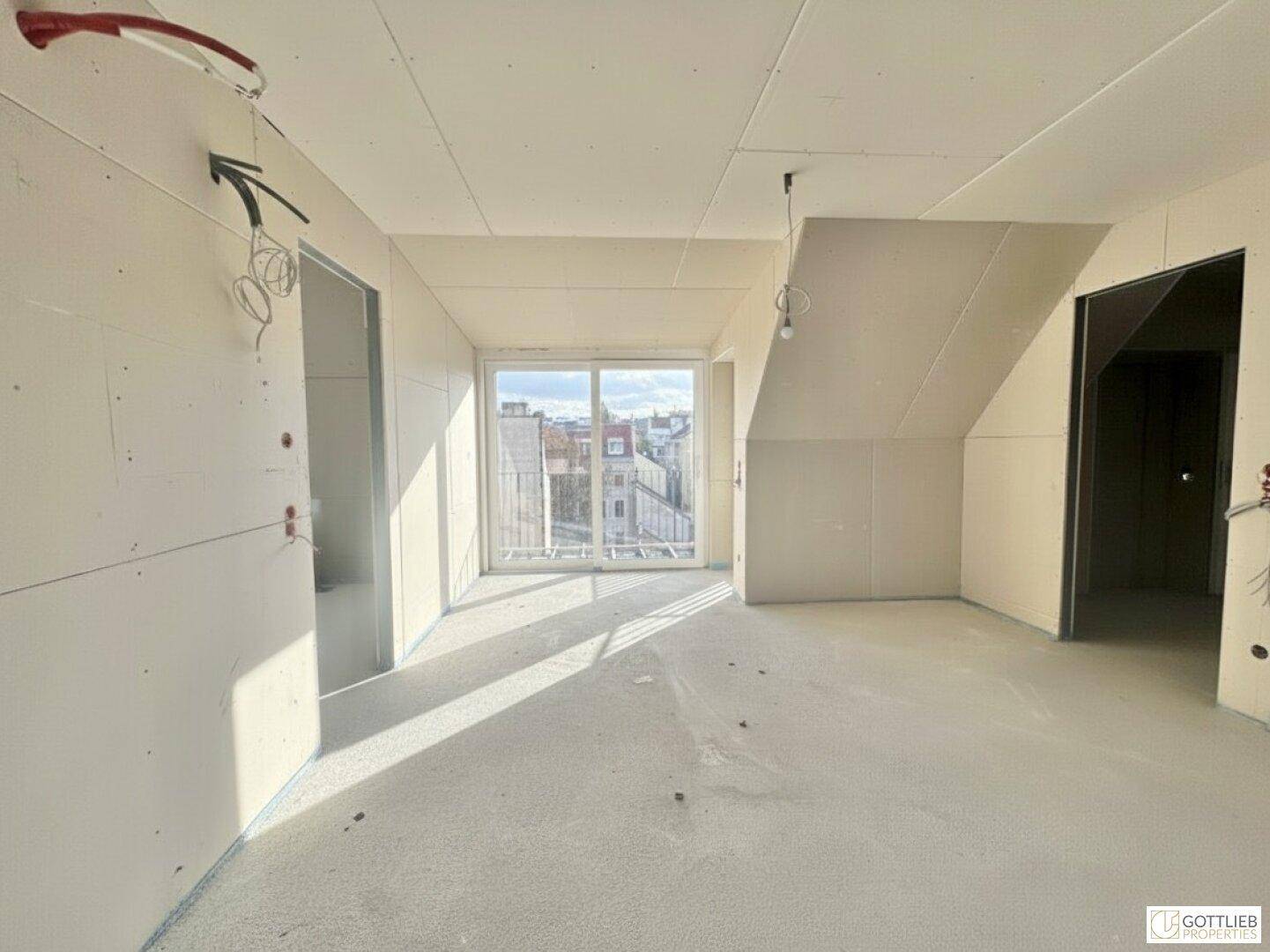 Heller Innenraum im Rohbau mit großer Schiebetür und Blick auf die umliegenden Gebäude.