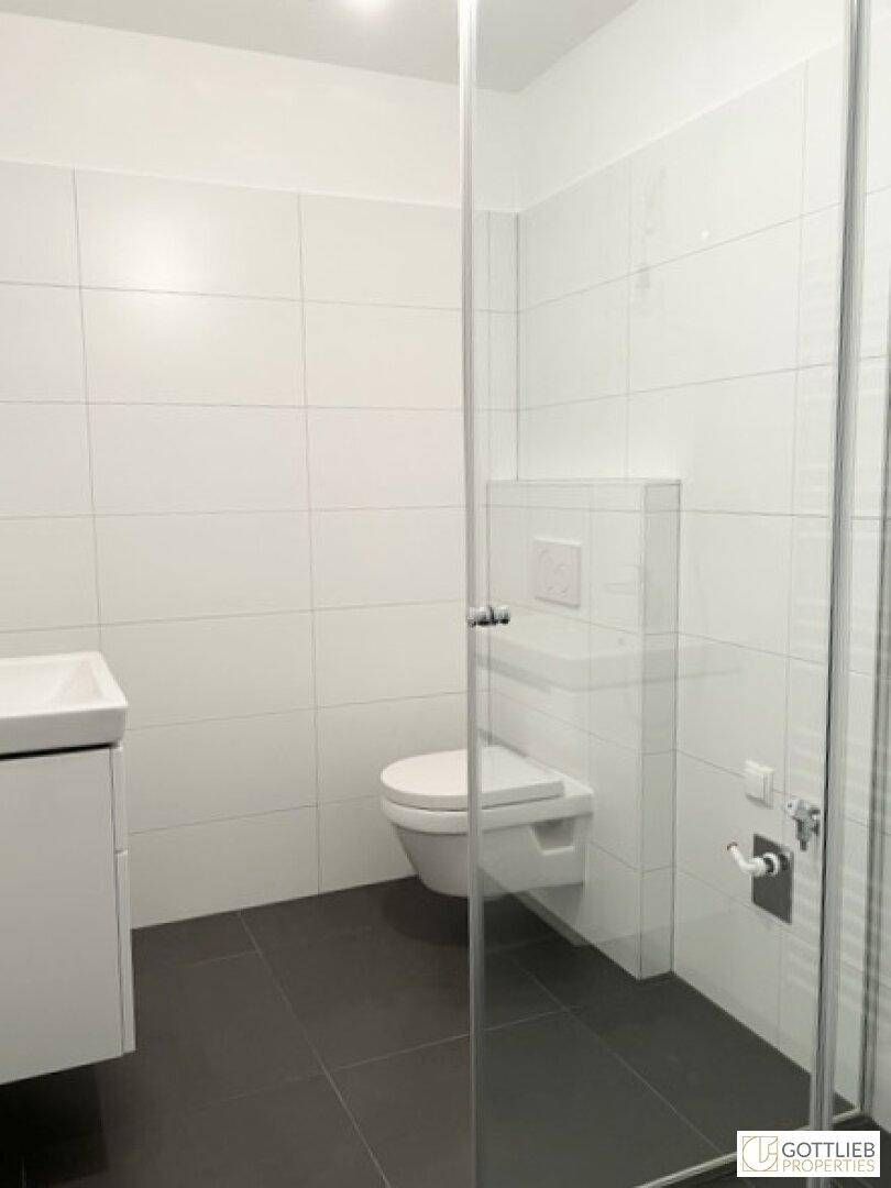 Modernes Badezimmer mit begehbarer Dusche, wandhängender Toilette und weißen Fliesen.
