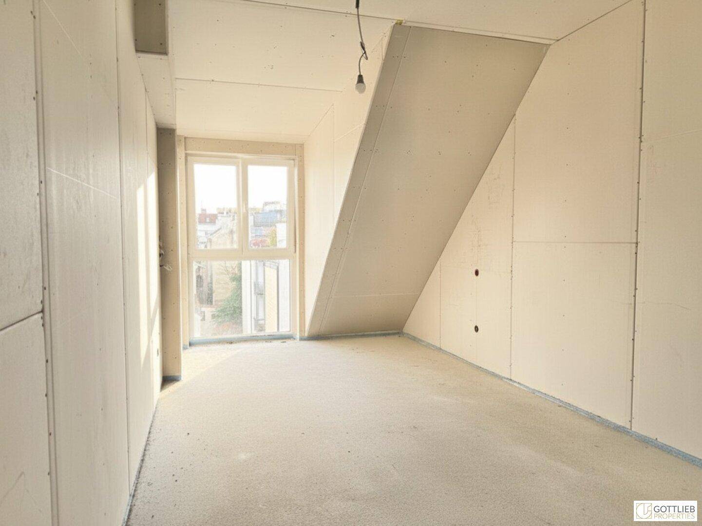 Unfertiger Raum mit großem Fenster und schräger Decke, bereit für den Innenausbau.