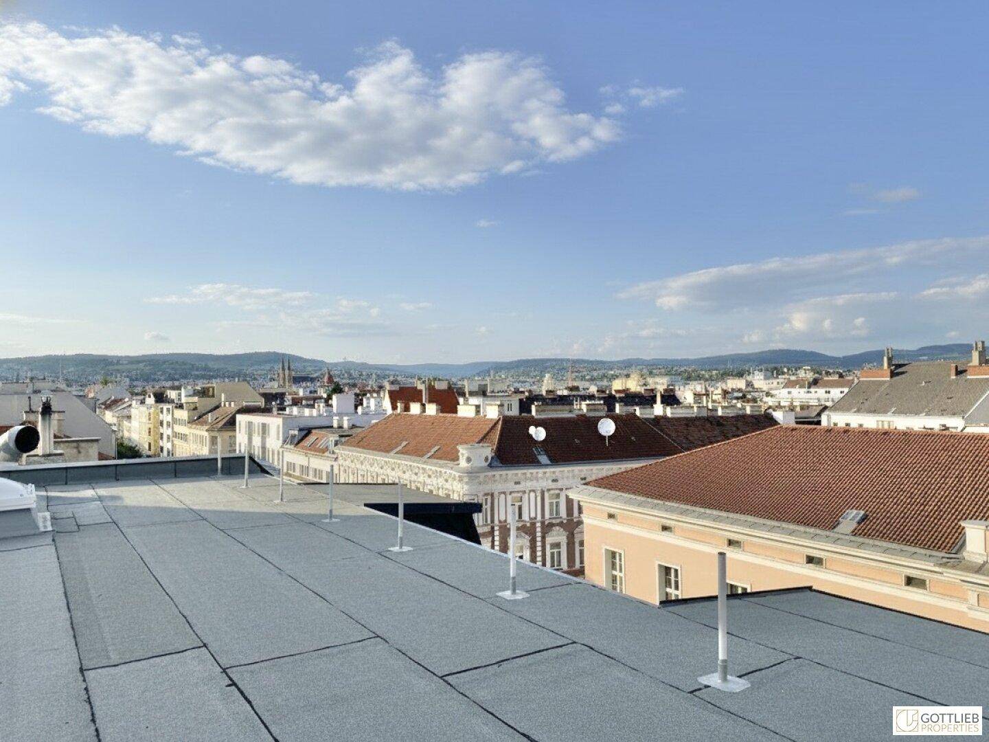 Panoramablick über die Stadt mit Dächern und grünen Hügeln am Horizont.