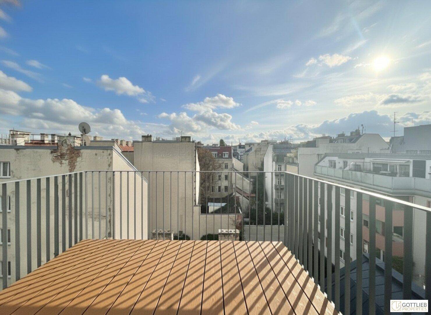 Sonniger Balkon mit Holzbelag, Metallgeländer und weitem Blick über die städtische Umgebung.