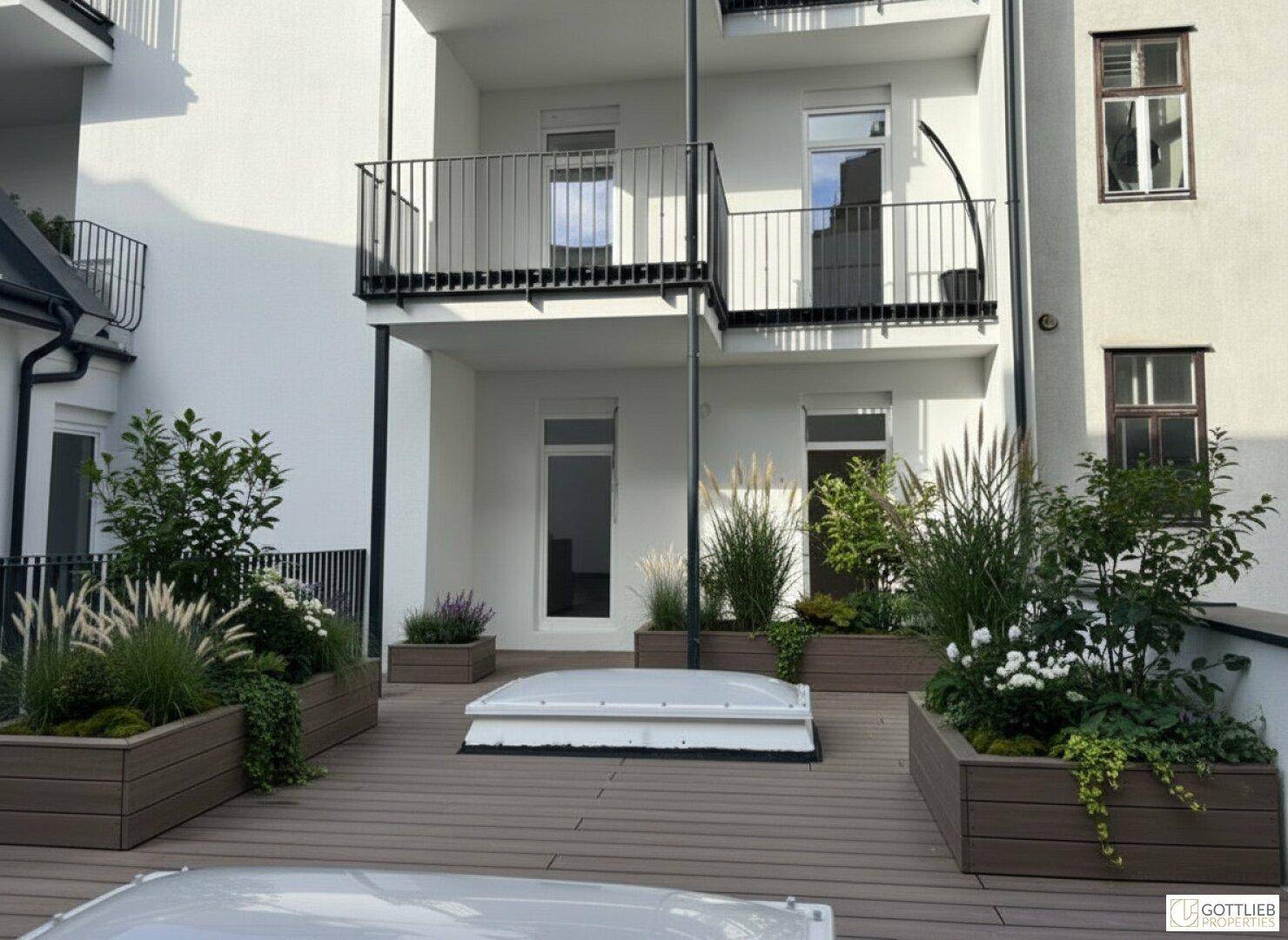 Begrünte Dachterrasse mit Holzbelag und Blick auf die moderne Gebäudefassade mit Balkonen.