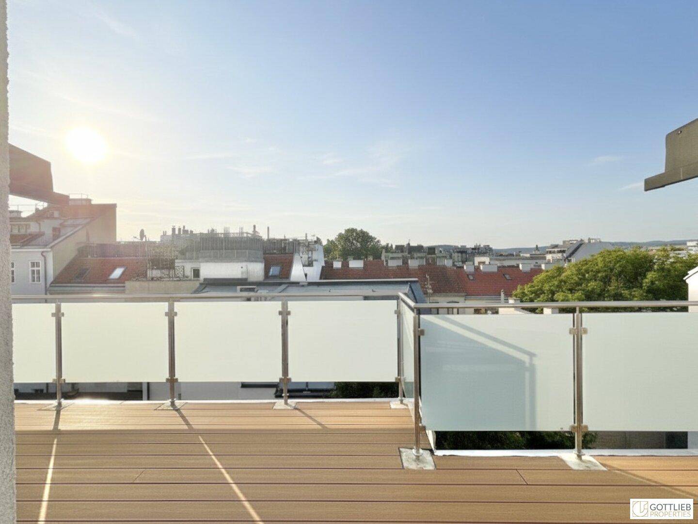 Sonnige Dachterrasse mit modernem Glasgeländer und Blick über die städtischen Dächer.