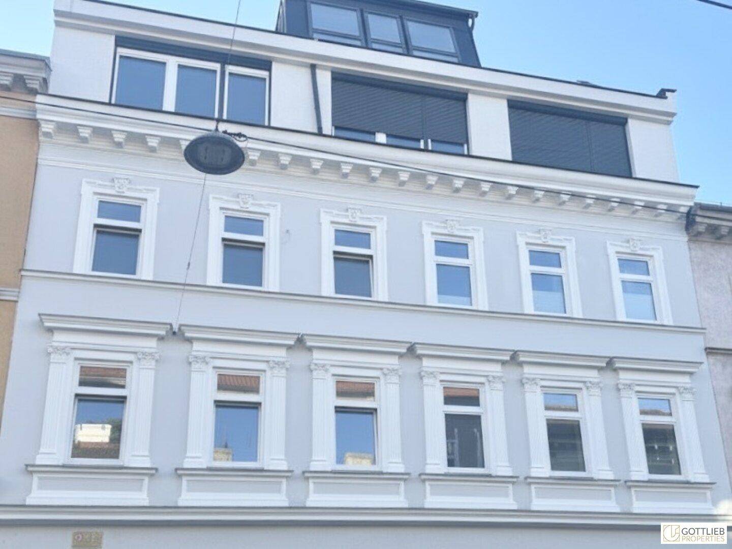 Historische Fassade eines Mehrfamilienhauses mit modernen Dachgeschossfenstern und Rollläden.