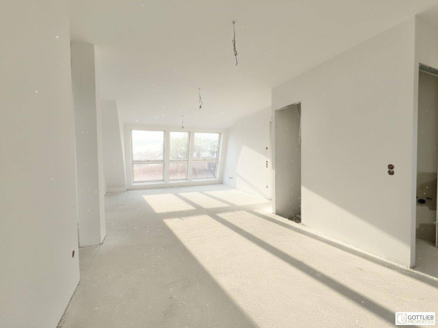 Heller, unmöblierter Wohnbereich im Dachgeschoss mit großen Fenstern und viel Tageslicht.