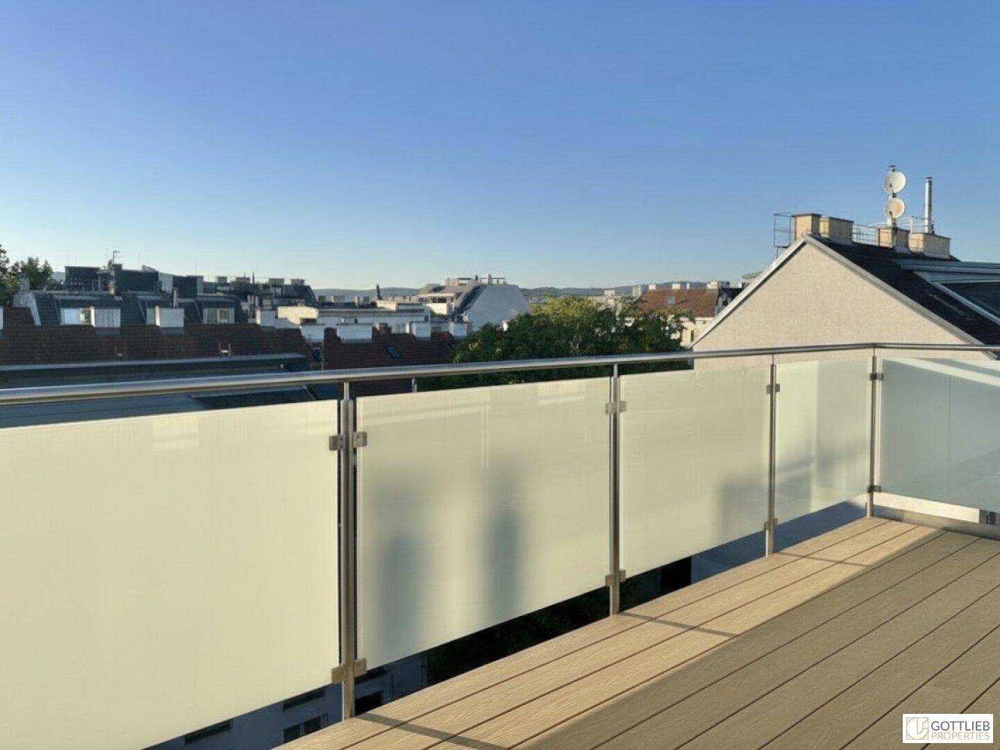Moderne Dachterrasse mit Holzboden und undurchsichtigem Glasgeländer, bietet Privatsphäre.