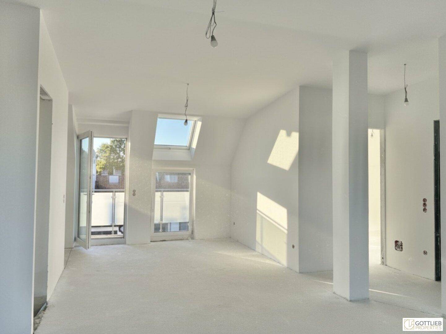 Großer, heller Wohnbereich im Dachgeschoss mit Zugang zu einem Balkon und Dachfenstern.