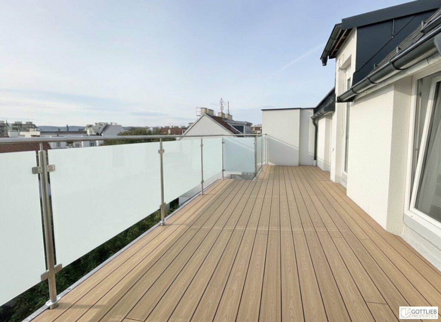 Weitläufige Dachterrasse mit Holzboden und Glasgeländer, ideal für sonnige Stunden.