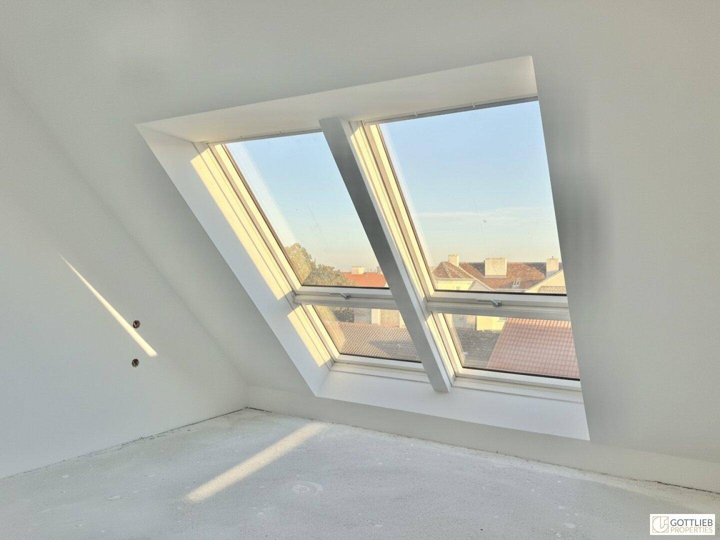 Lichtdurchfluteter Dachgeschossraum mit schrägen Wänden und Blick über die Dächer.
