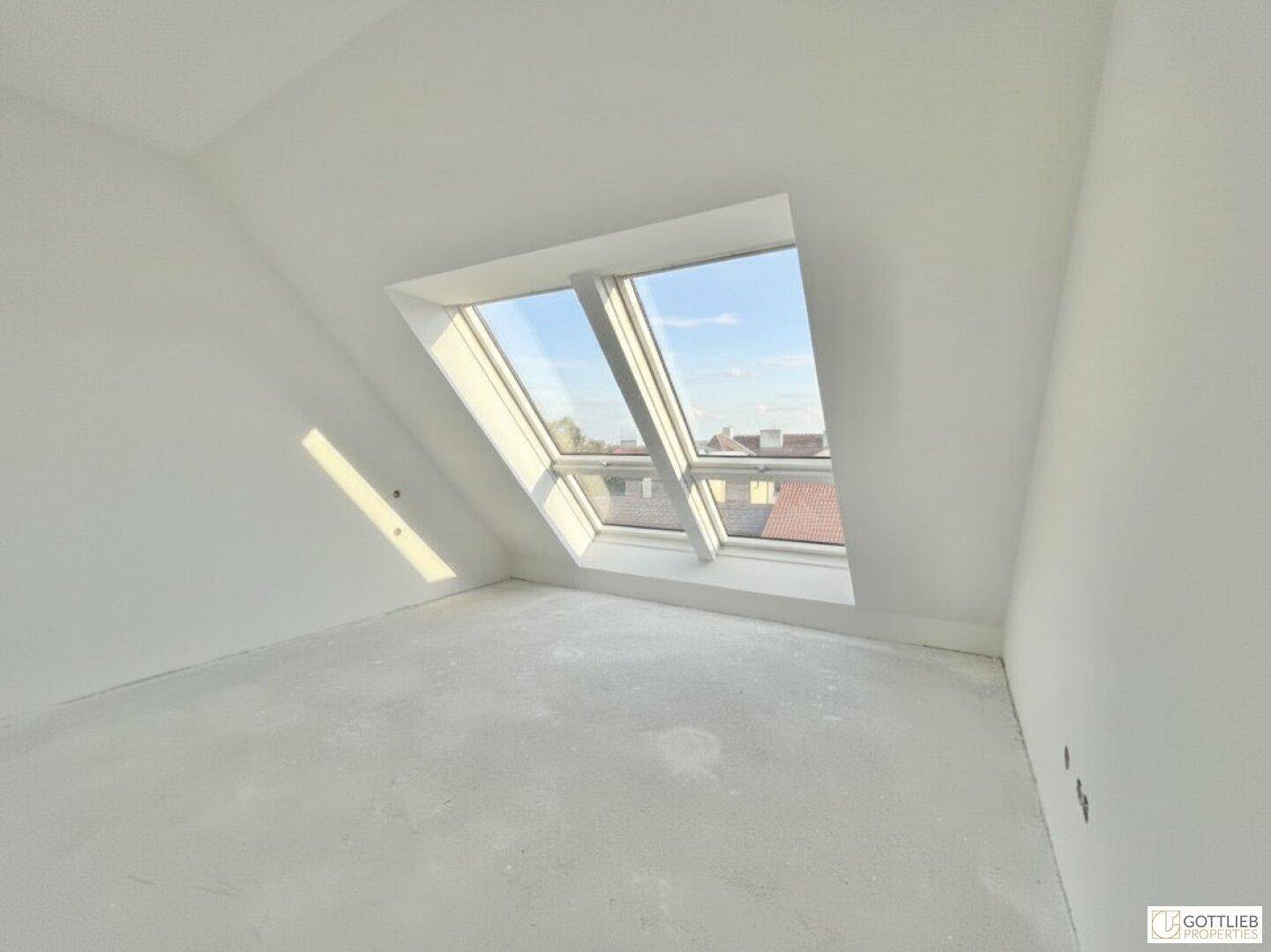 Lichtdurchfluteter Dachgeschossraum mit schrägen Wänden und Blick auf die Umgebung.