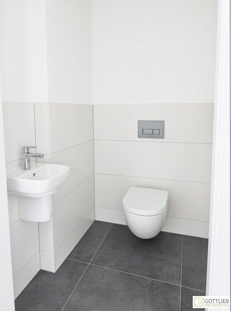 Modernes Gäste-WC mit wandhängender Toilette, kleinem Waschbecken und dunklen Bodenfliesen.