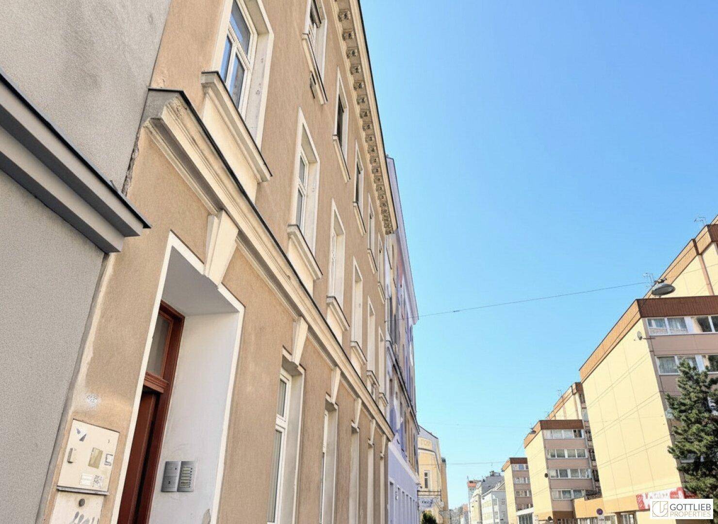Seitenansicht eines Wohngebäudes mit Blick auf die Straße und weitere Gebäude unter blauem Himmel.