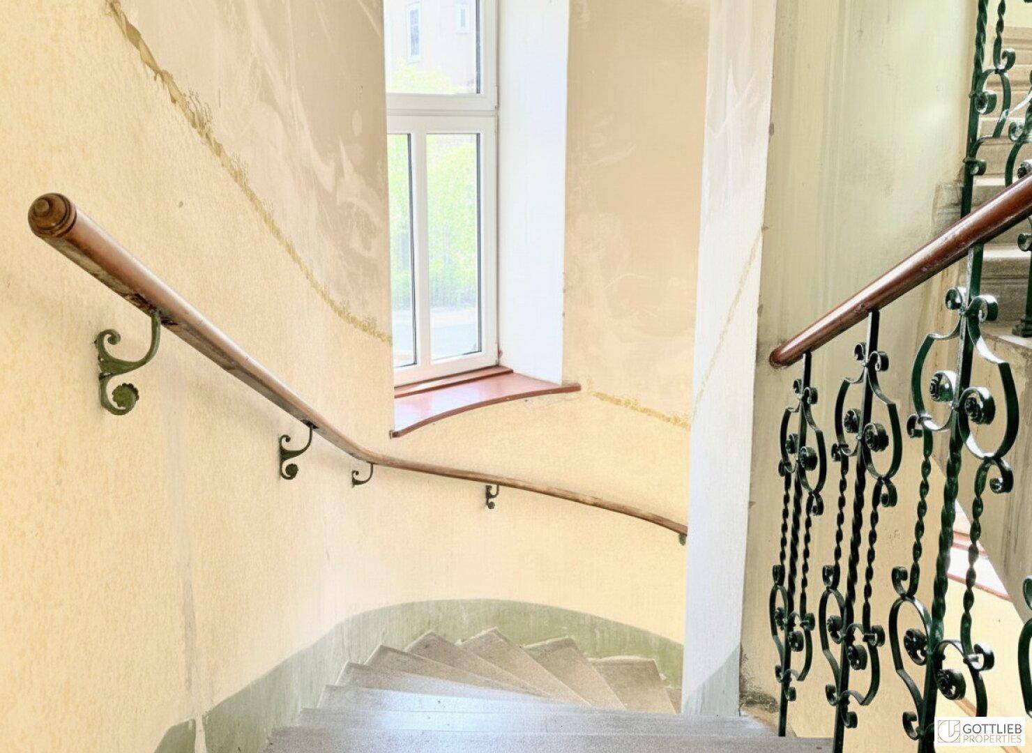 Detailansicht einer geschwungenen Treppe mit Holzhandlauf und Fenster, das natürliches Licht hereinlässt.