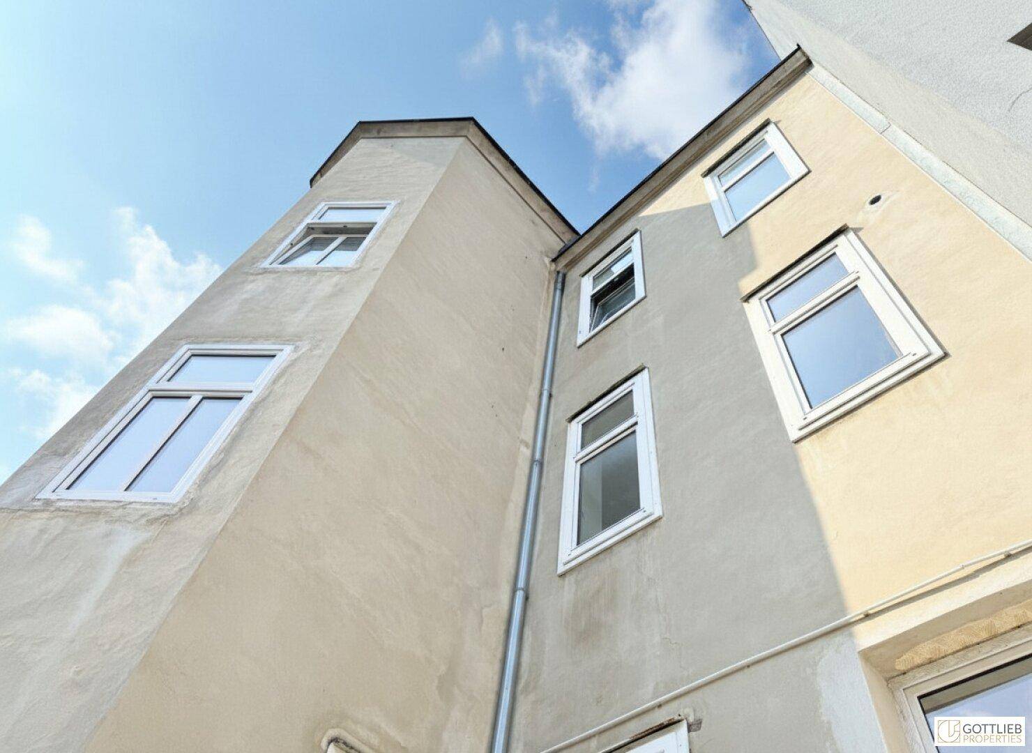 Schräge Ansicht eines Gebäudes mit mehreren Fenstern und einer schlichten Fassade unter blauem Himmel.