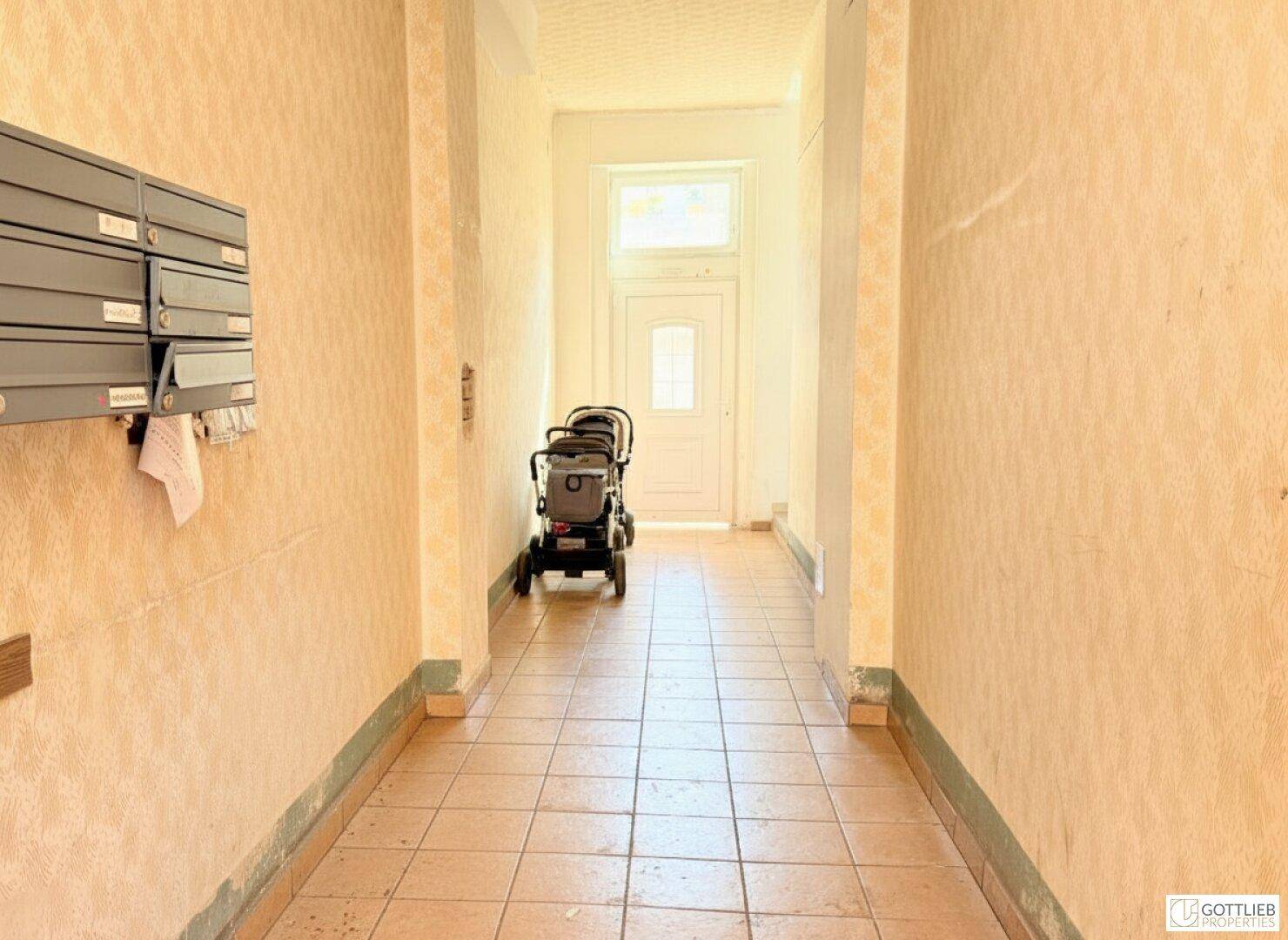 Heller Eingangsbereich mit Fliesenboden, Briefkästen an der Wand und einem Kinderwagen.