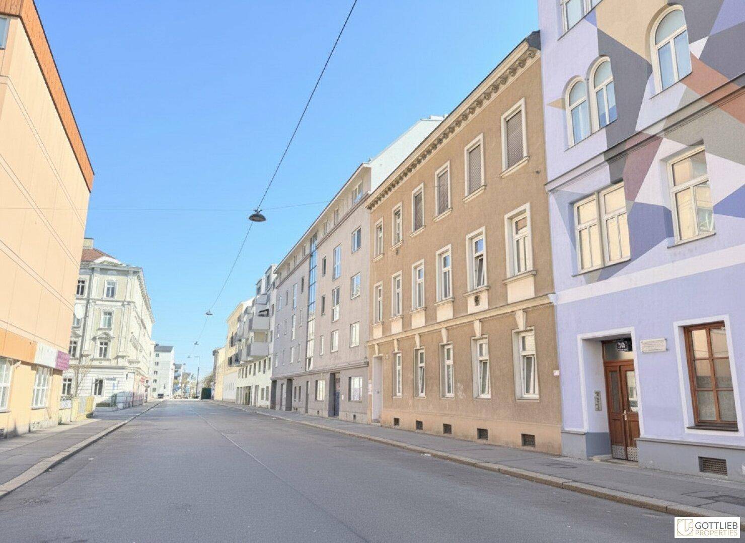 Weitläufige Straßenansicht mit mehreren Gebäuden unterschiedlicher Farben und einem klaren Himmel.
