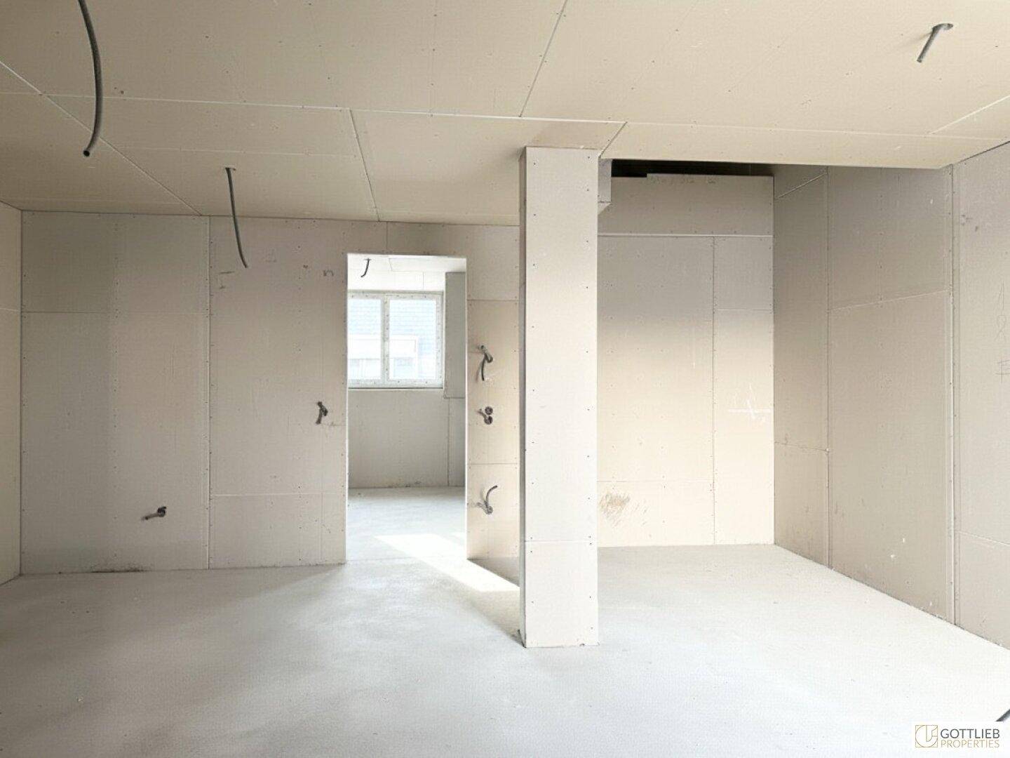 Unfertiger Innenraum mit Trockenbauwänden und Betonboden, bereit für den weiteren Ausbau.
