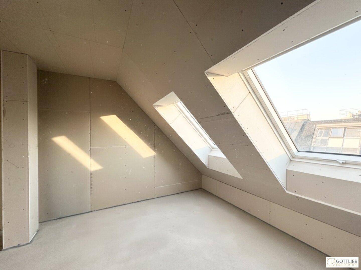 Unfertiger Dachraum mit Trockenbauwänden, Betonboden und mehreren Dachfenstern für viel Licht.