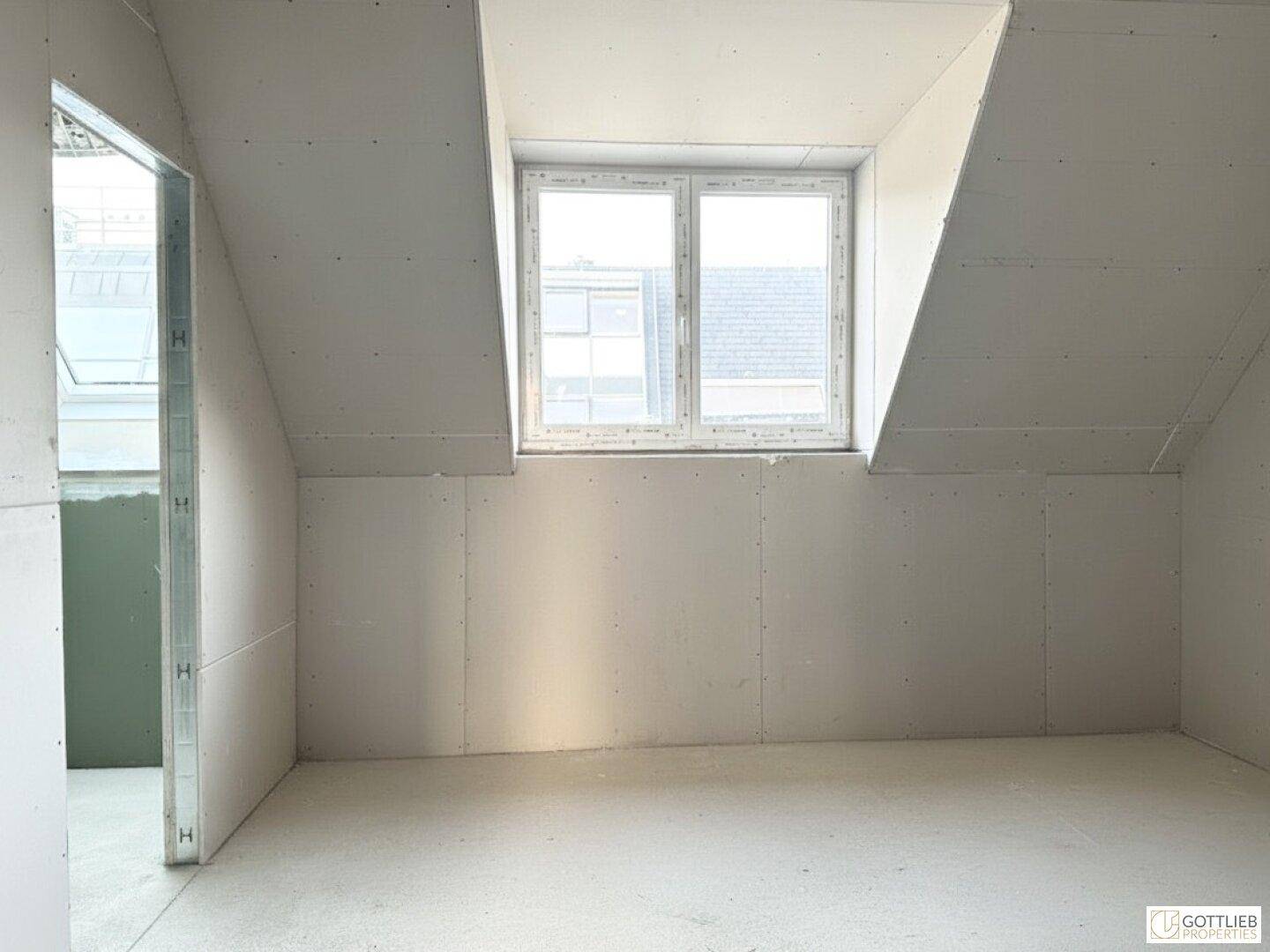 Unfertiger Dachraum mit schrägen Wänden und einem Fenster, das Tageslicht hereinlässt.