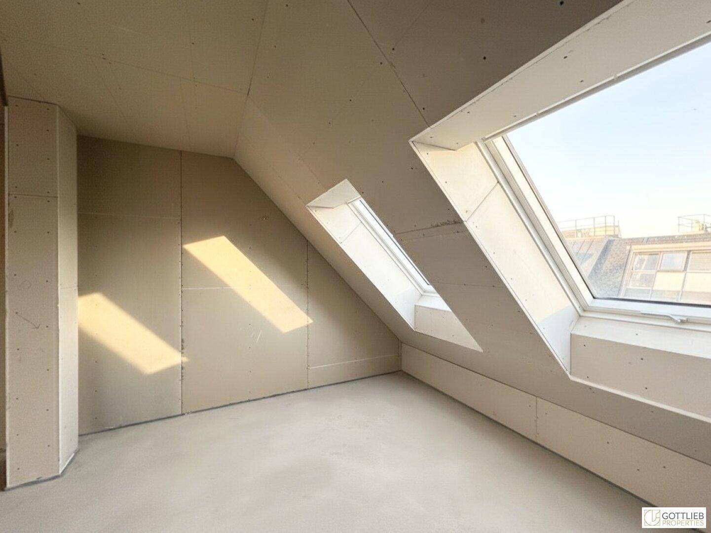 Unfertiger Dachraum mit schrägen Wänden und mehreren Dachfenstern für viel Licht.