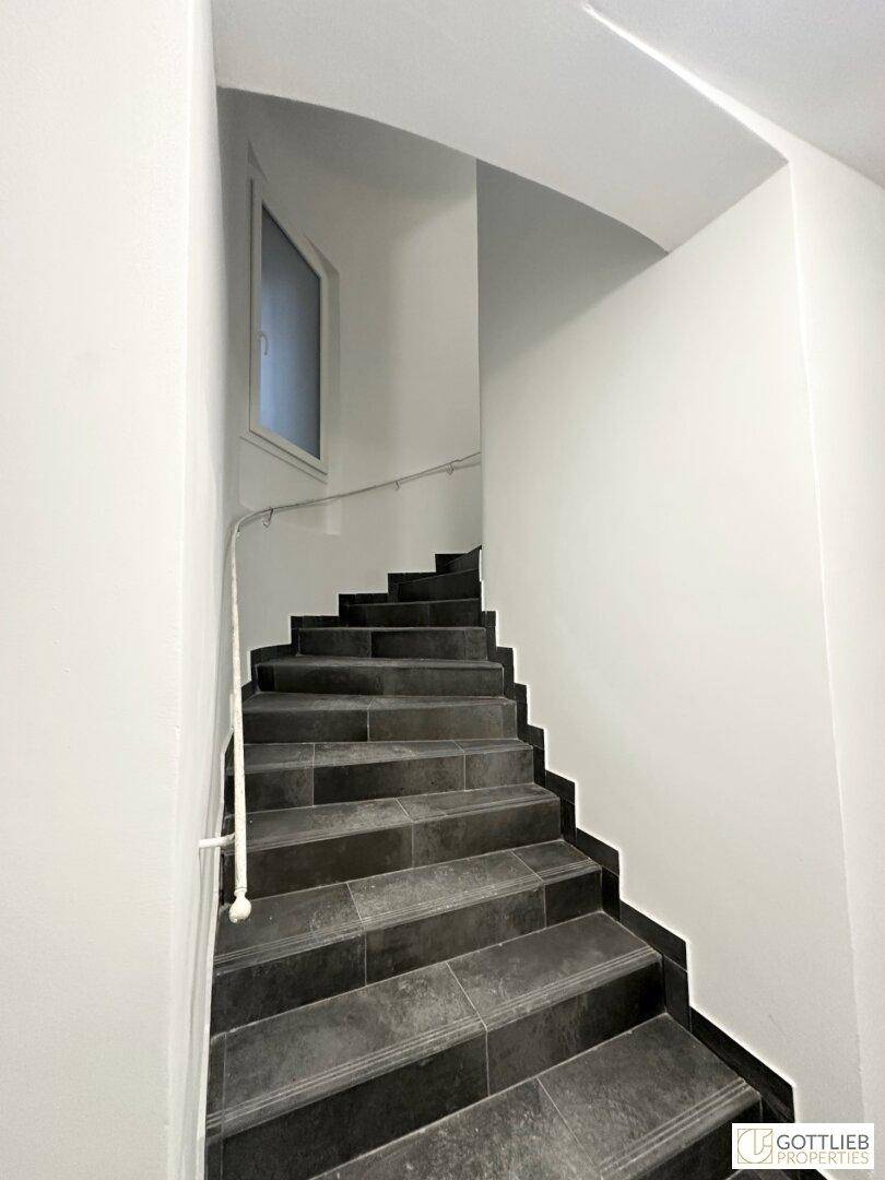 Wendeltreppe mit dunklen Fliesen und weiß gestrichenen Wänden in einem Treppenhaus.
