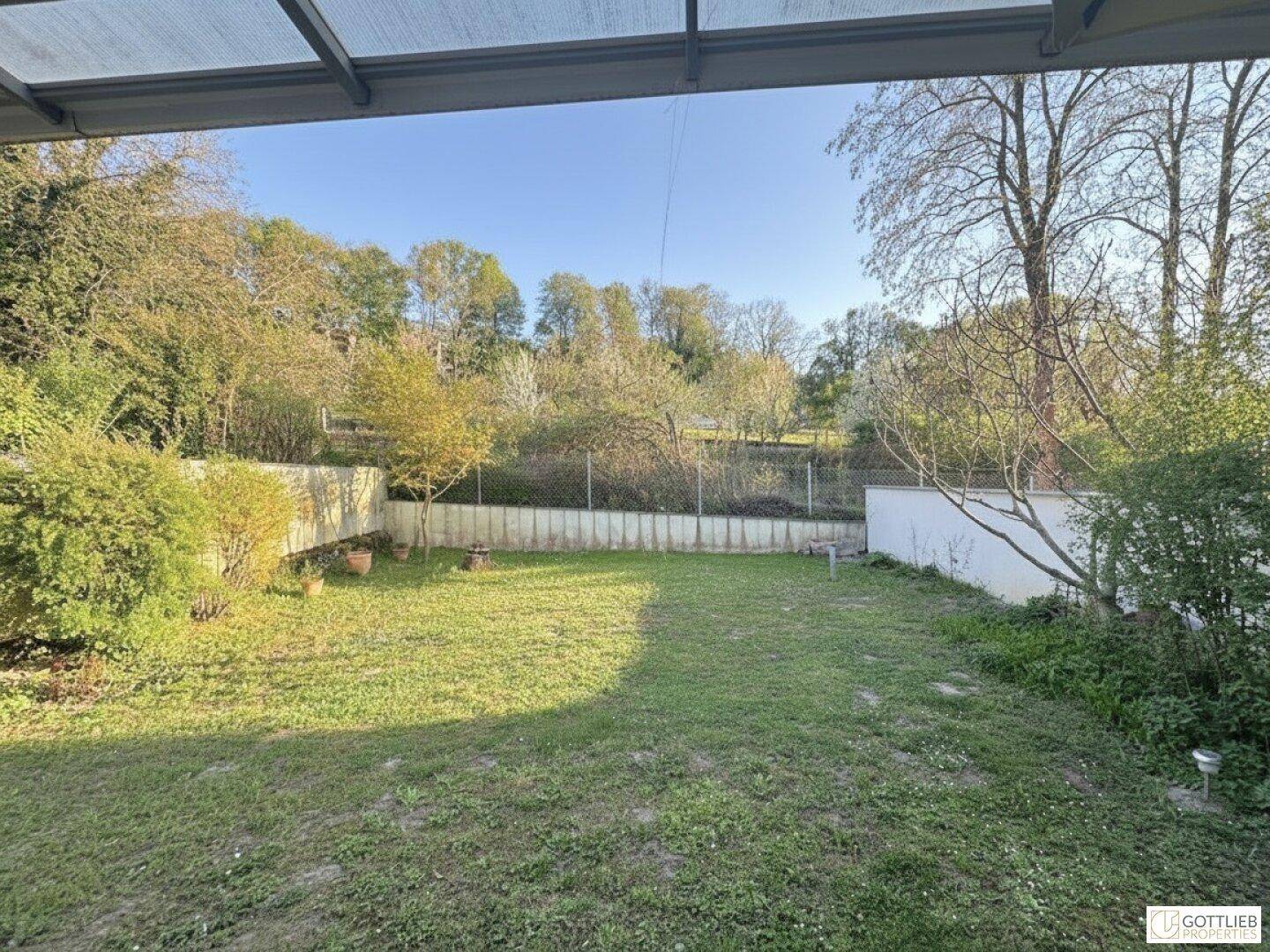 Weitläufiger Garten mit Rasenfläche, umgeben von Bäumen und Sträuchern an einem sonnigen Tag.
