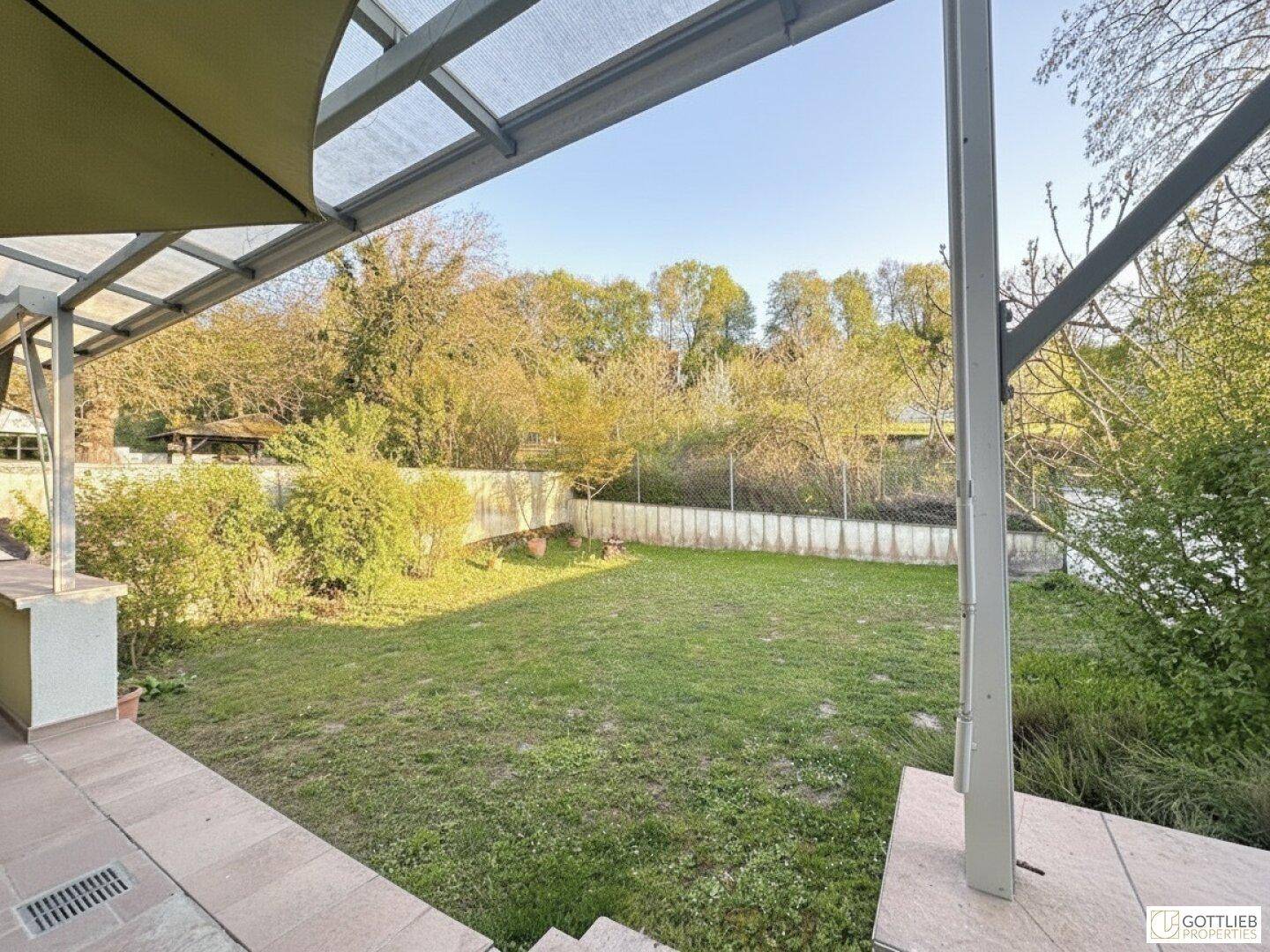 Blick von der überdachten Terrasse in den weitläufigen Garten mit viel Grün.