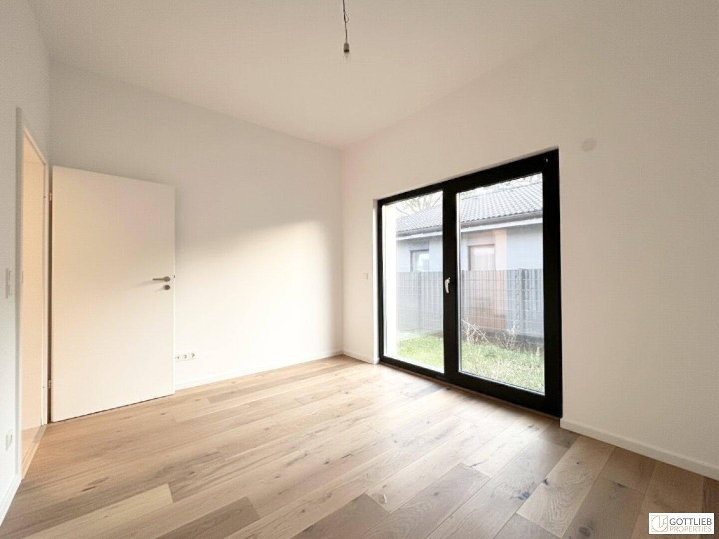 Helles Schlafzimmer mit Parkettboden und großen Fenstern, die den Raum mit Licht durchfluten.