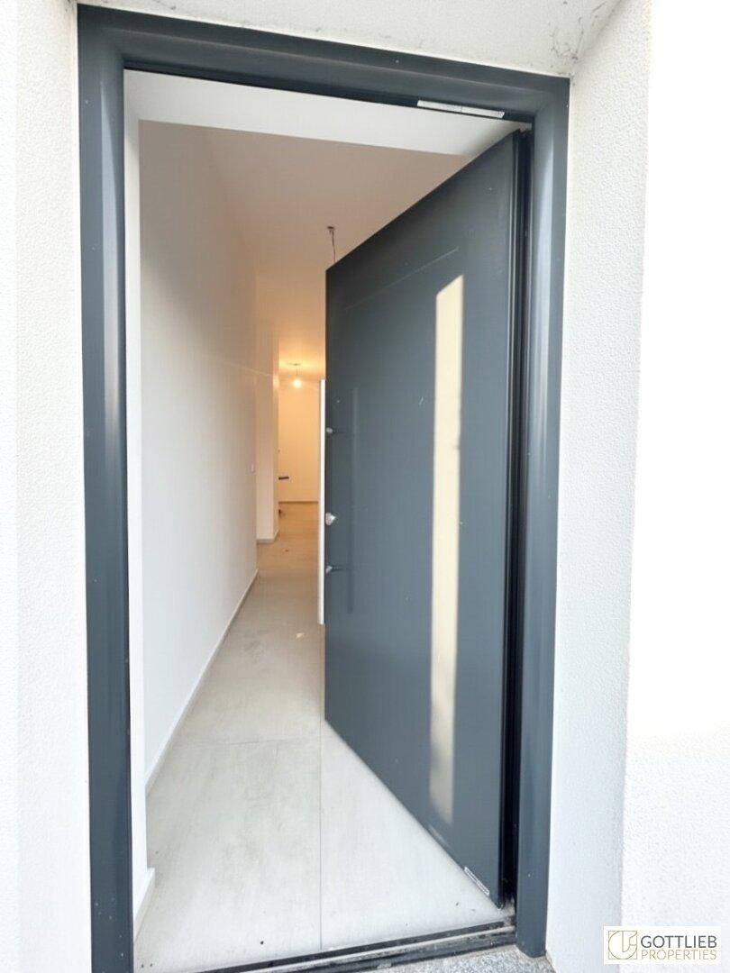 Offene Eingangstür führt in einen hellen Flur mit Fliesenboden und modernem Design.