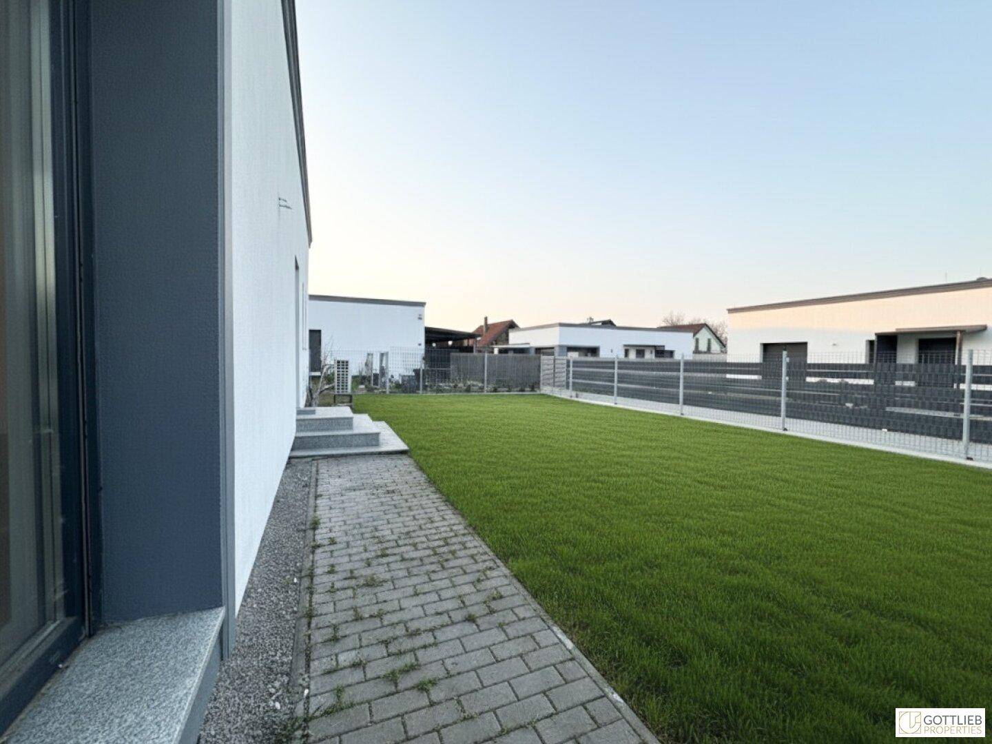 Großer, gepflegter Rasenbereich neben dem Haus mit einem gepflasterten Weg und Zaun.