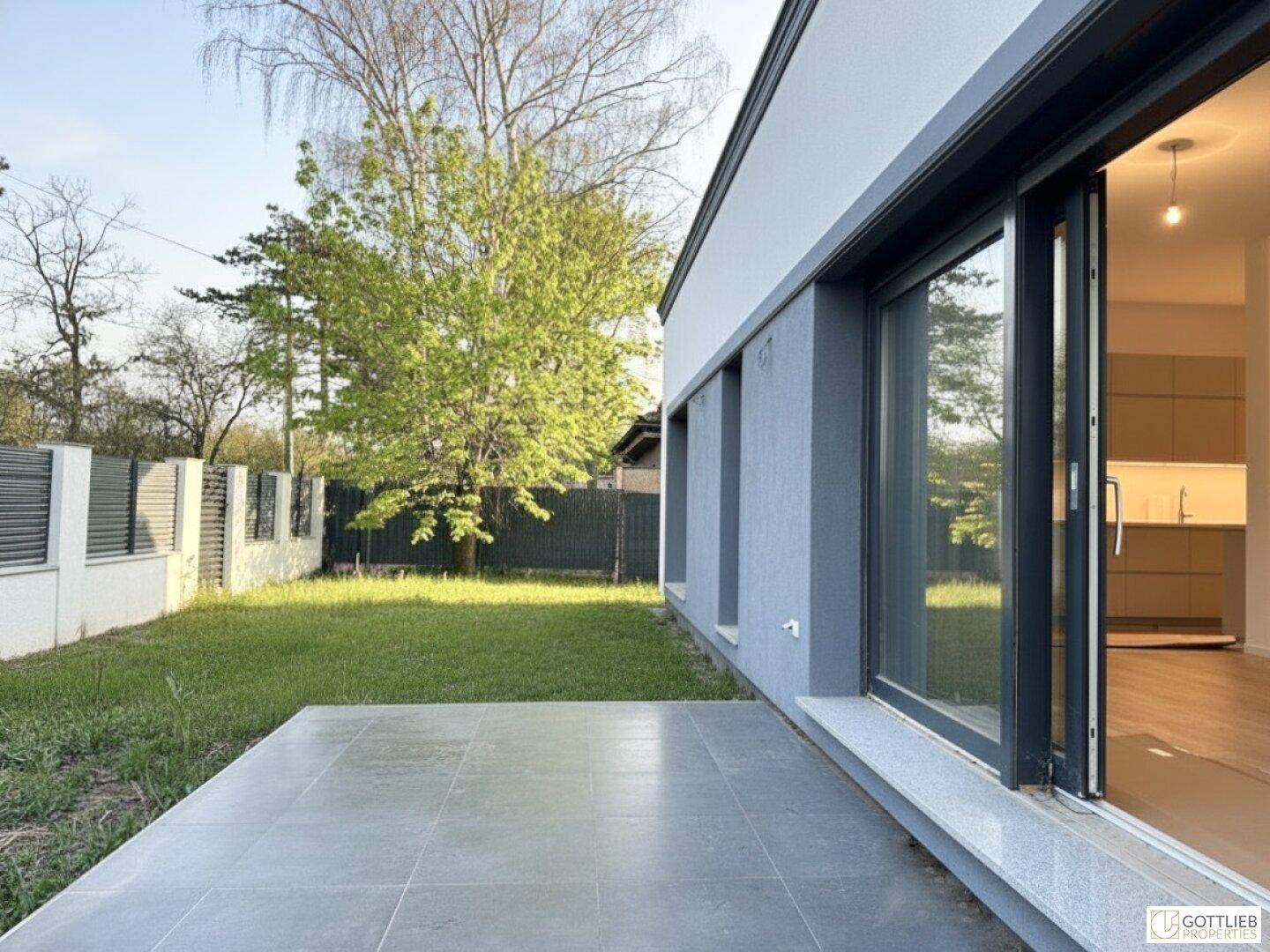 Moderne Terrasse mit Fliesenboden und Zugang zum Garten, daneben ein Blick in die Küche.